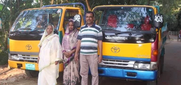 방글라데시에서 그라민 은행의 소액 대출을 통해 구입한 노란색 트럭 두 대 앞에 서 있는 남성과 여성들의 모습. 자립에 성공한 대출자들의 자부심 있는 표정.