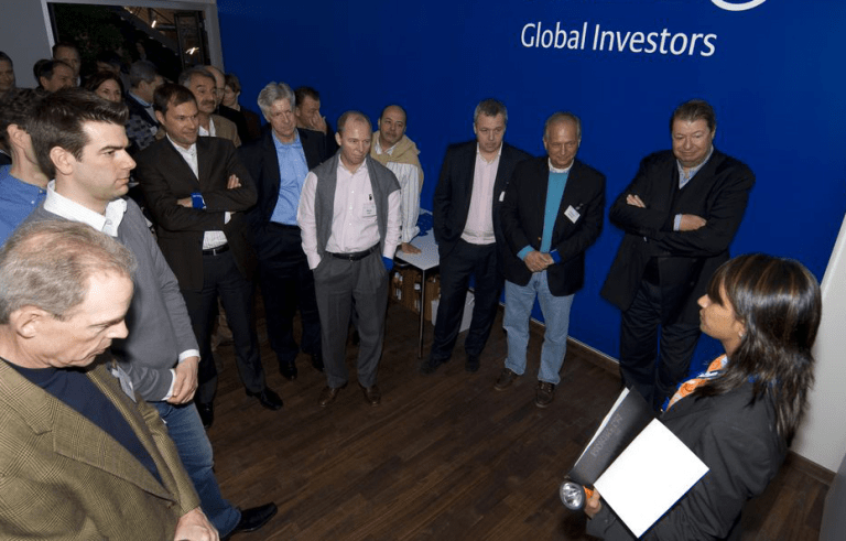 다이알로그 소셜 엔터프라이즈(DSE)의 '어둠 속의 대화' 전시 현장에서 시각 장애인 가이드가 'Global Investors'라고 적힌 벽면 앞에서 글로벌 전문가 및 투자자들을 대상으로 리더십과 커뮤니케이션 세미나를 진행하는 모습. 장애를 능력으로 재정의한 임팩트 비즈니스의 실증적 사례.