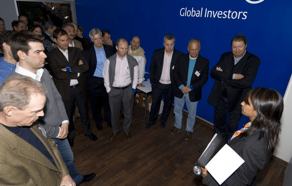 다이알로그 소셜 엔터프라이즈(DSE)의 '어둠 속의 대화' 전시 현장에서 시각 장애인 가이드가 'Global Investors'라고 적힌 벽면 앞에서 글로벌 전문가 및 투자자들을 대상으로 리더십과 커뮤니케이션 세미나를 진행하는 모습. 장애를 능력으로 재정의한 임팩트 비즈니스의 실증적 사례.