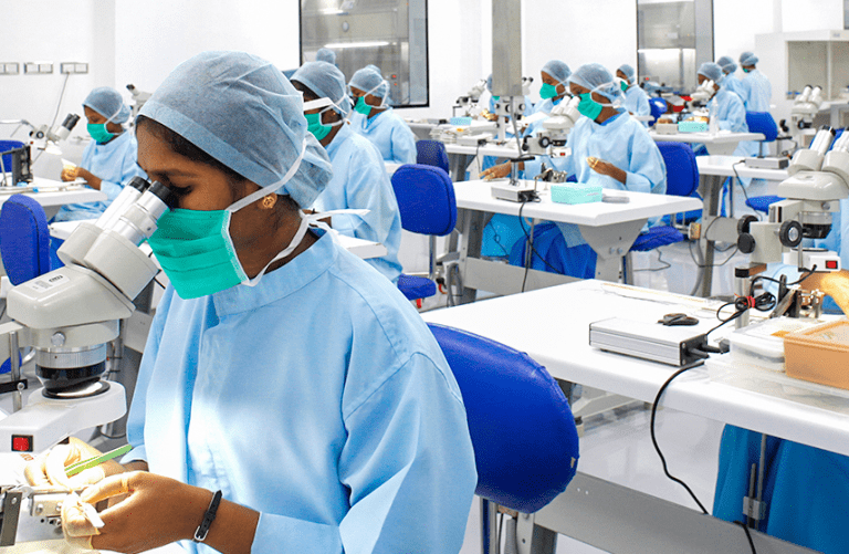 인도의 아라빈드 안과병원(Aravind Eye Hospital)에서 푸른색 위생복과 마스크를 착용한 수많은 의료진이 현미경을 사용하여 전문적인 수술 혹은 정밀 작업을 수행하는 모습. 분업화와 표준화된 의료 시스템을 상징하는 사진.