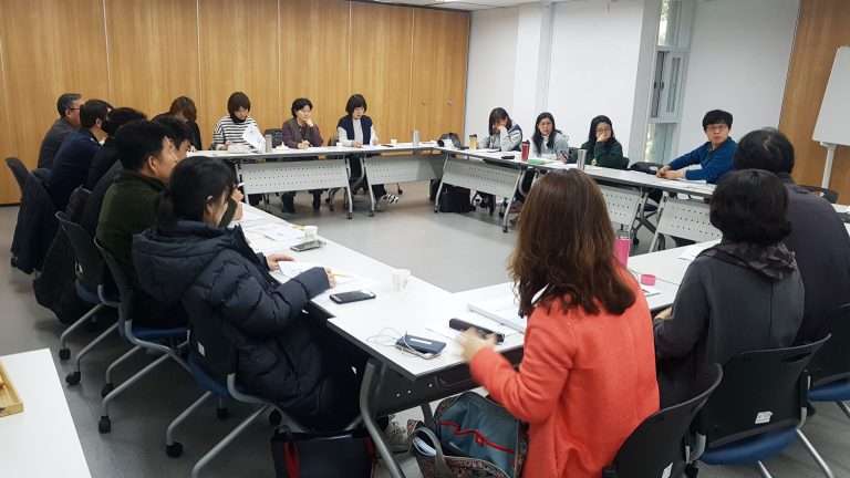 밝은 회의실에서 남녀 실무자들이 테이블에 둘러앉아 자료를 검토하며 진지하게 토론하고 있는 모습. 조직 내 ESG 전략 수립을 위한 내부 협의 및 전문가 코칭 현장을 상징하는 사진.