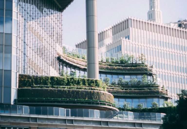 현대적인 고층 유리 빌딩의 외벽을 따라 층층이 조성된 풍성한 녹색 테라스와 수직 정원의 전경. 글로벌 공시 규제 강화에 발맞추어 기업의 구조적 투명성과 지속가능성을 시각화한 이미지.