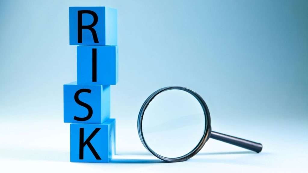 RISK'라는 글자가 세로로 새겨진 파란색 큐브 블록 탑과 그 옆에 놓인 돋보기 클로즈업 사진. 기업의 잠재적 그린워싱 리스크를 면밀히 조사하고 검증하는 과정을 직관적으로 상징함.